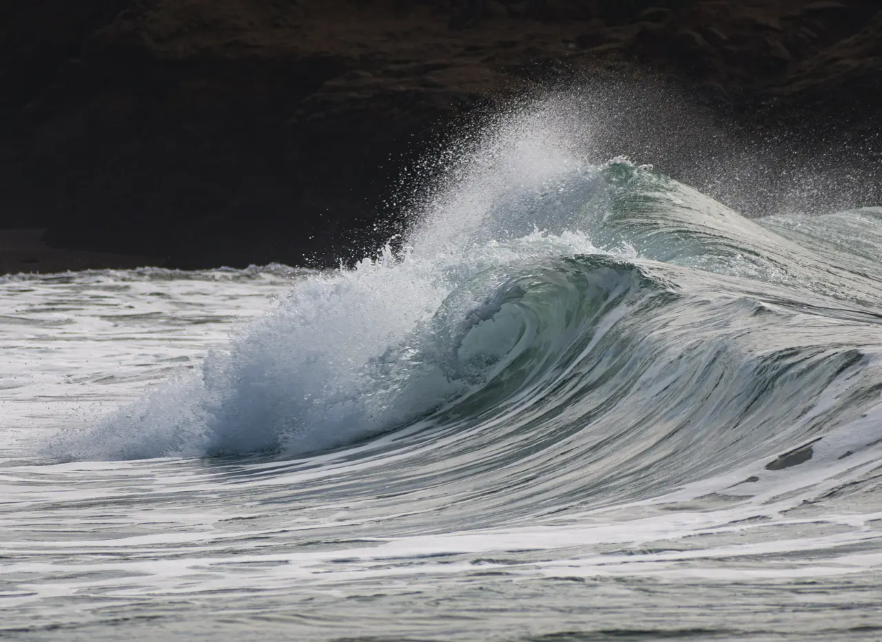 A blue wave folding into white spray